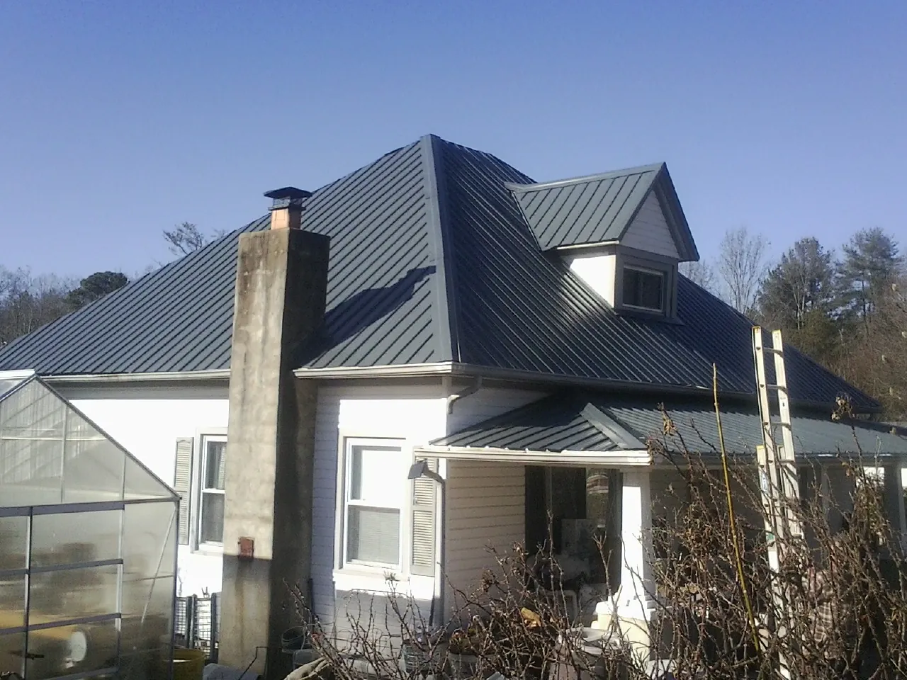 Dark blue standing seam metal roof on a white farmhouse with dormer — Slate & Tile Roof Repair by Roofing Brothers in Surry