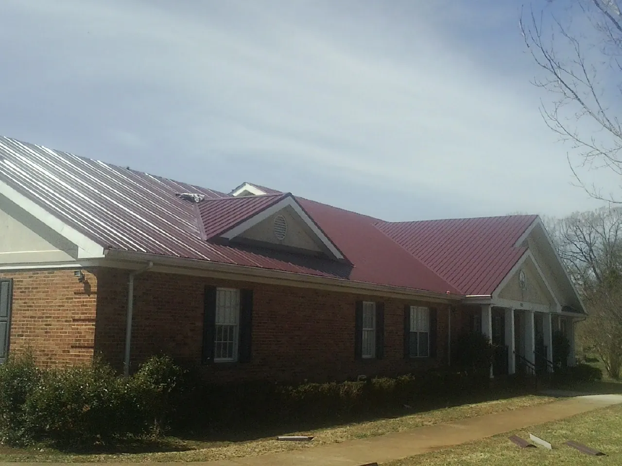 Red metal roof with gabled entries on a long brick building, from a Hail Damage Roof Repair job in Surry
