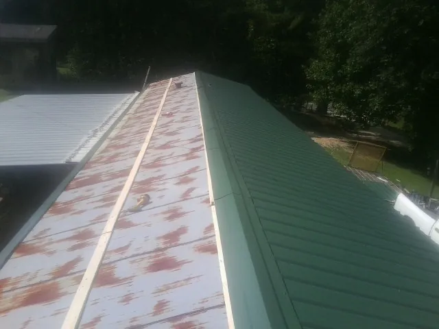 Old rusted panels beside newly installed green metal roofing — Wind Damage Roof Repair by Roofing Brothers in Surry