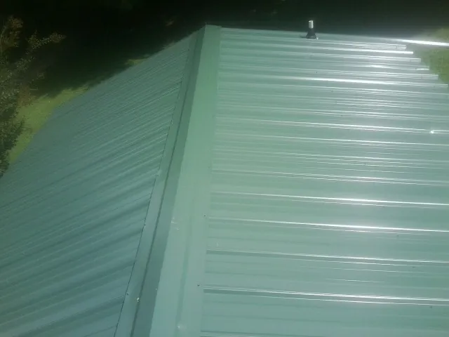 New green metal panels meeting at the ridge of a roof — Flat Roof Repair work by our crew in Surry