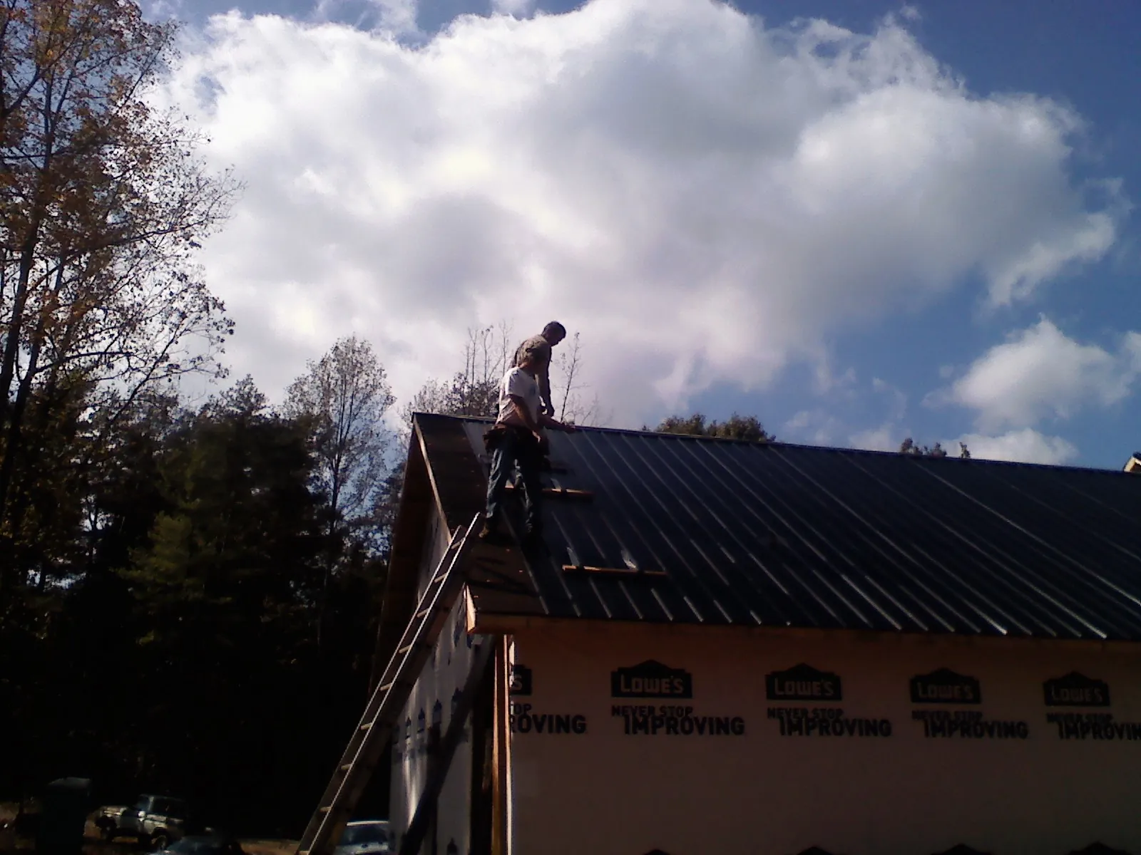 Roofer fastening dark metal panels high against a cloudy sky, from a Roof Inspection job in Surry