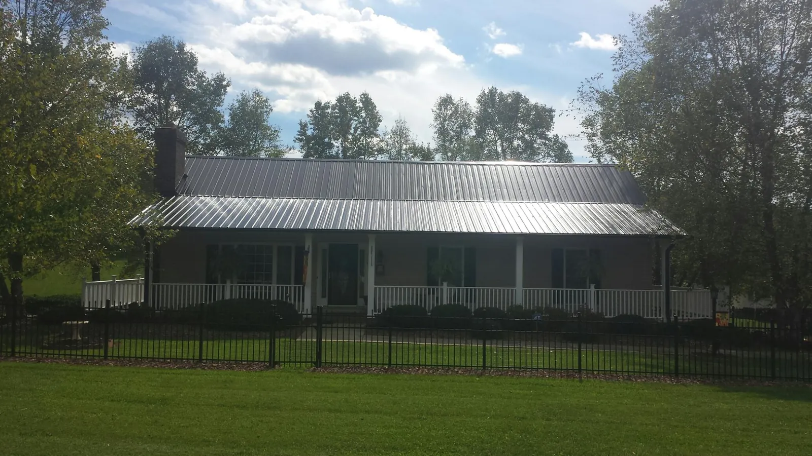 Gray metal roof on a brick ranch with a full width front porch — Gutter Guard Installation work by our crew in Surry
